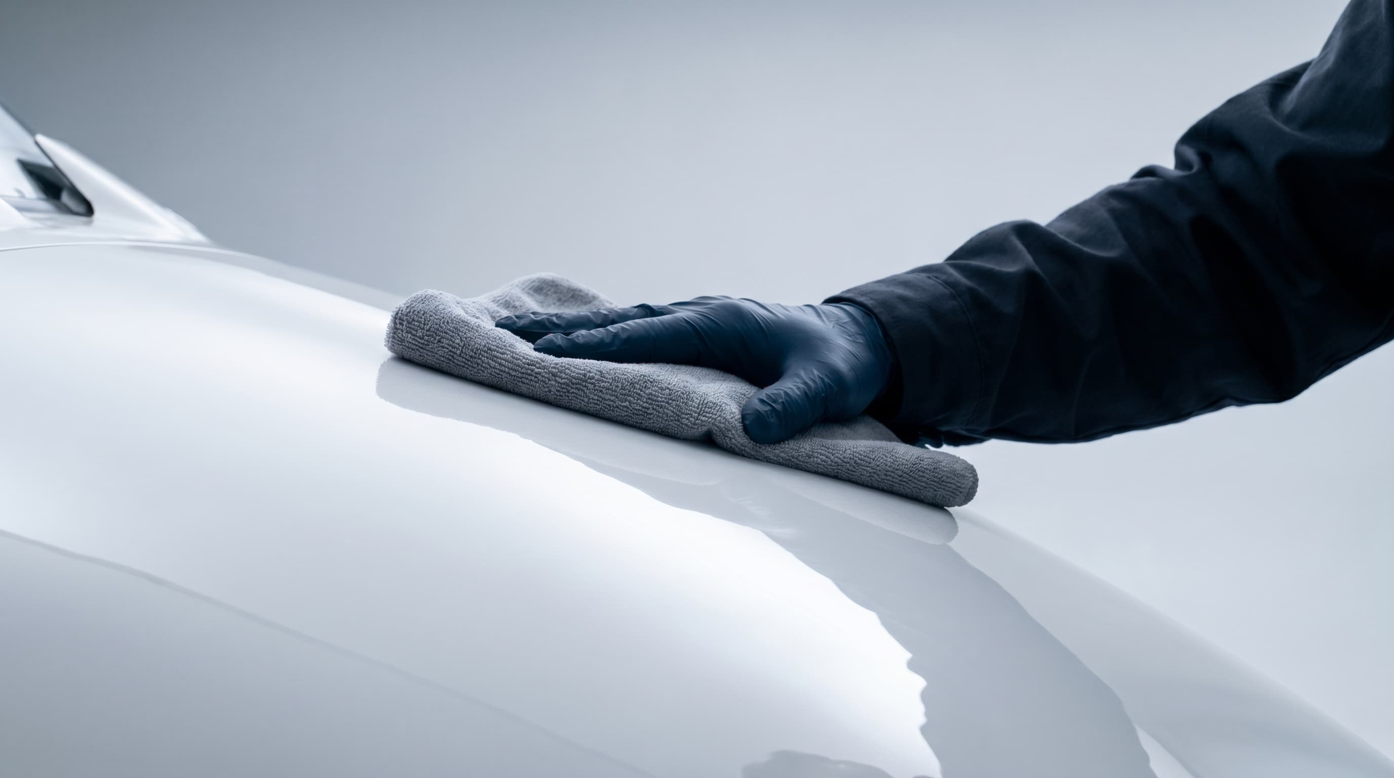 Detailer's gloved hand working a microfiber towel across a glossy white aircraft panel