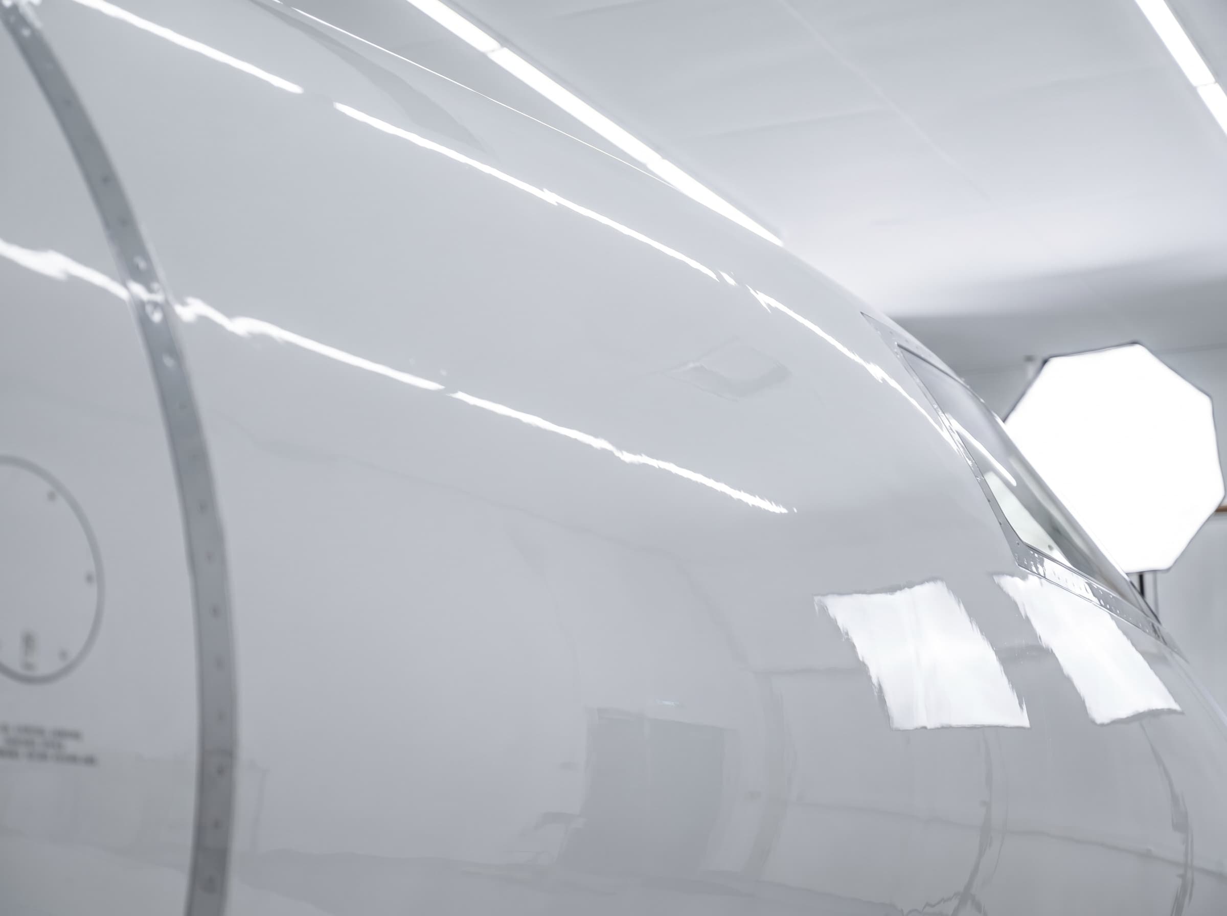 Mirror-gloss white aircraft paint reflecting hangar lighting after polishing